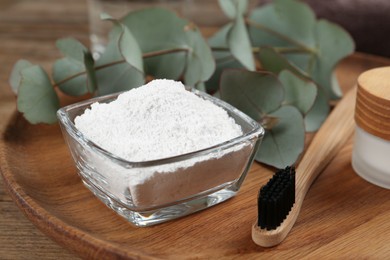 Photo of Tooth powder, brush and eucalyptus on wooden tray, closeup