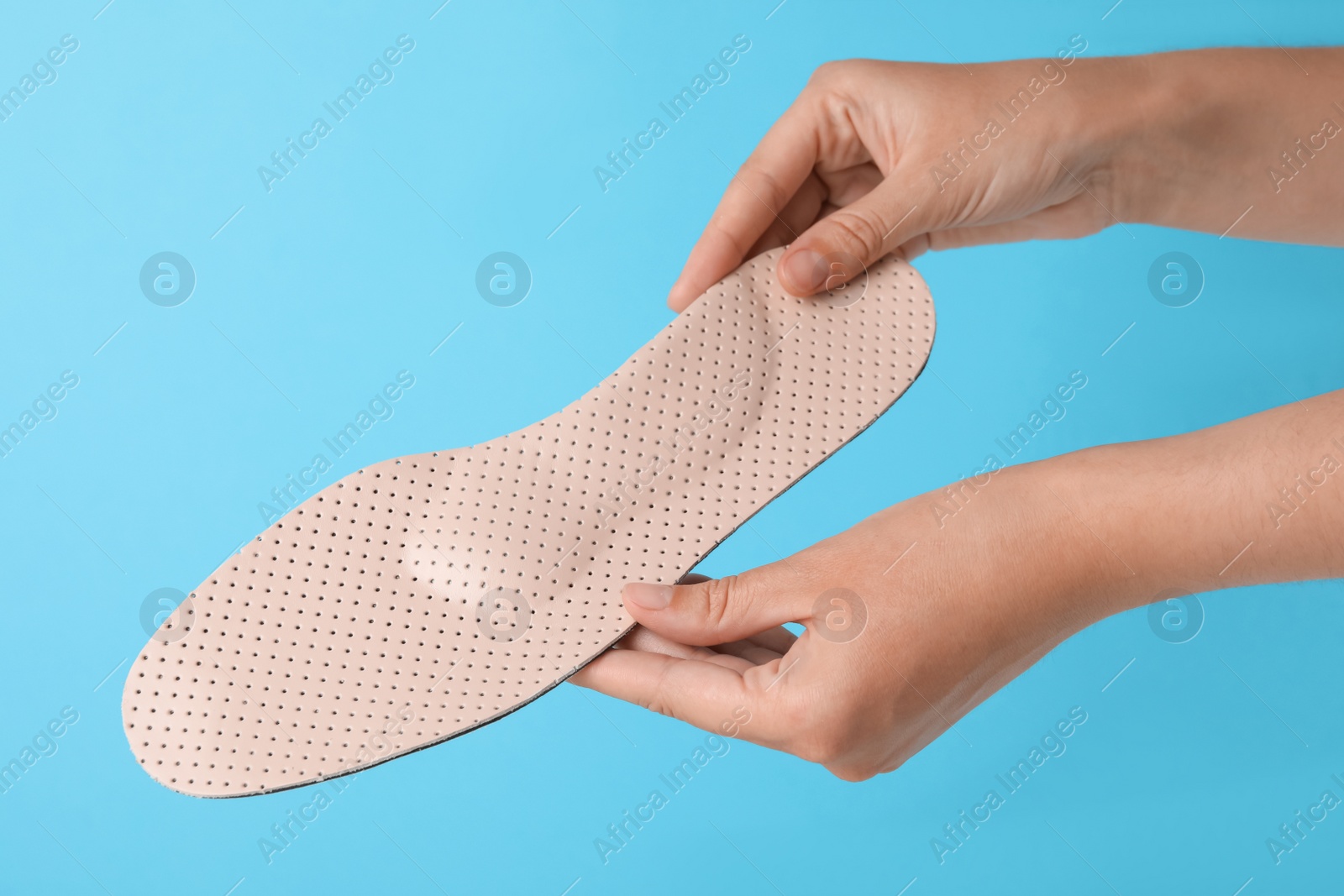 Photo of Woman holding beige orthopedic insole on light blue background, closeup