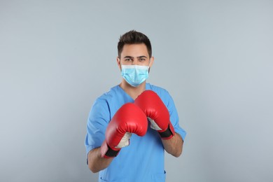 Photo of Doctor with protective mask and boxing gloves on light grey background. Strong immunity concept