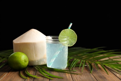 Photo of Jar with fresh coconut water and lime on table against black background