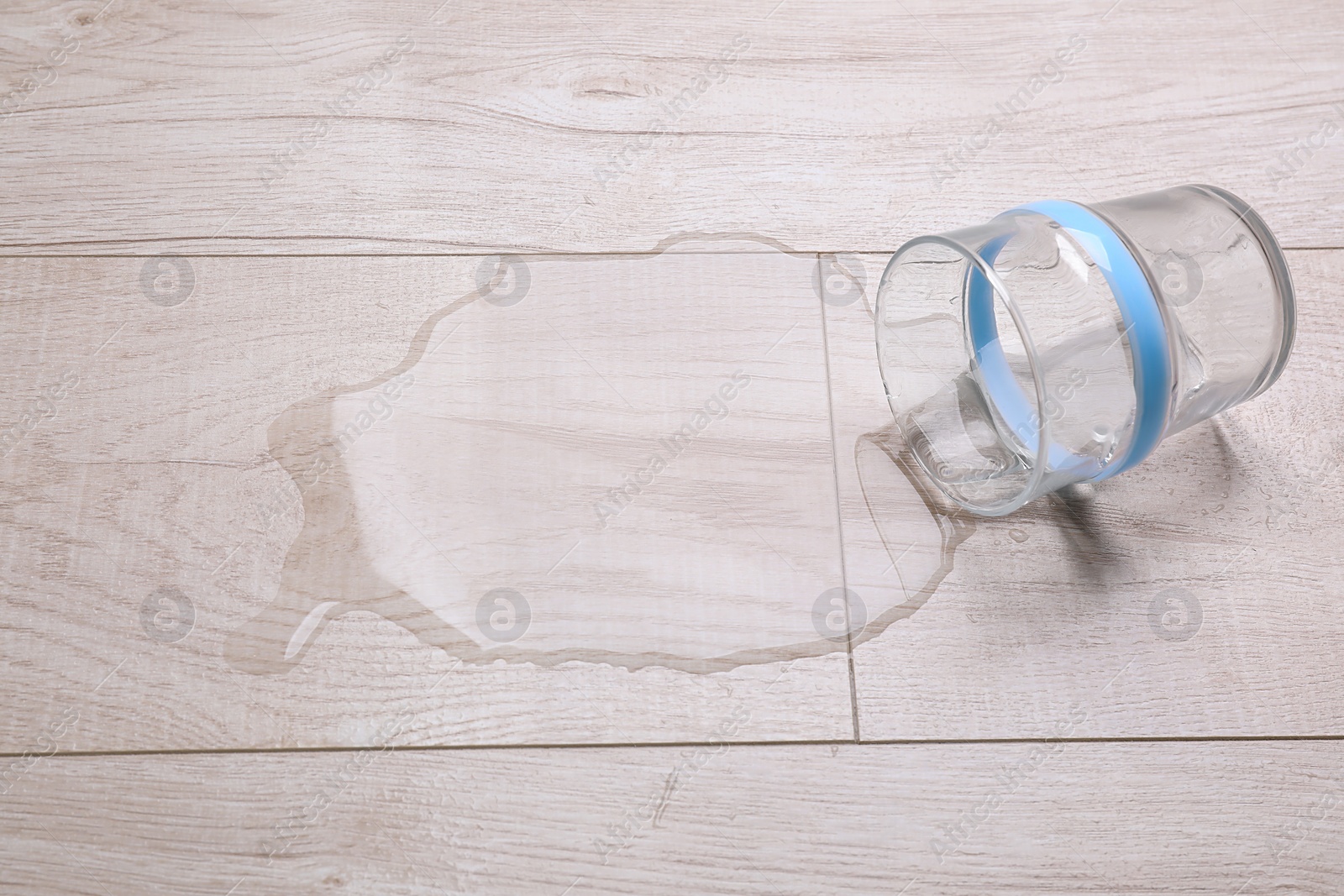 Photo of Glass with spilled water on wooden floor
