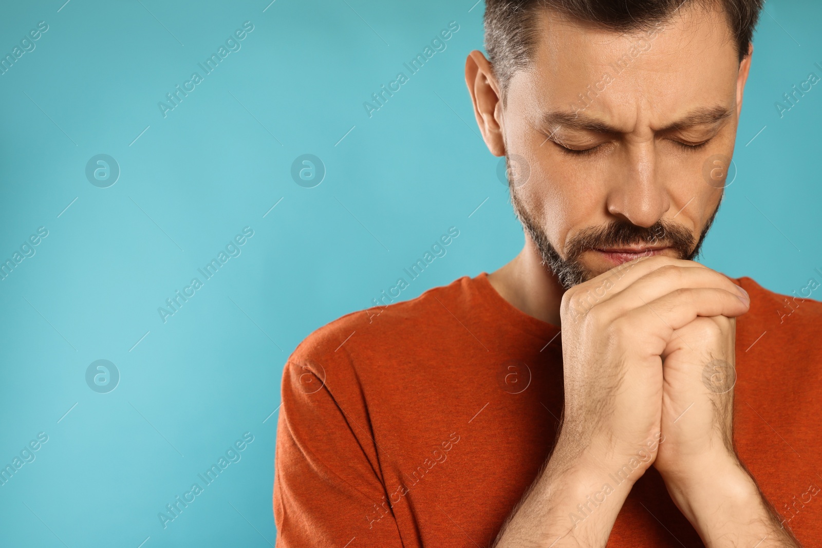 Photo of Man with clasped hands praying on turquoise background. Space for text