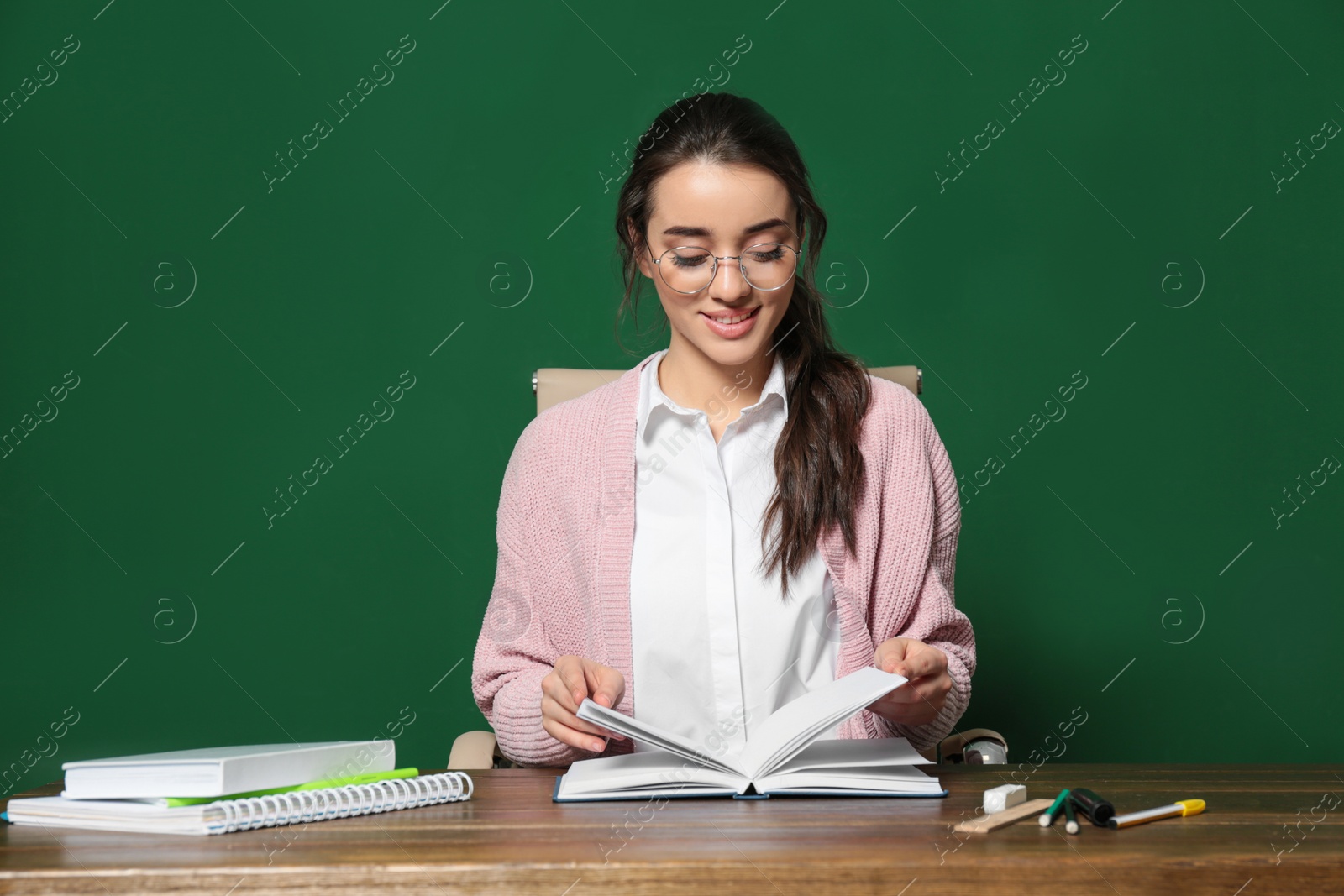 Photo of Portrait of beautiful young teacher sitting at table near chalkboard