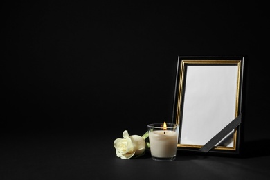 Photo of Funeral photo frame with ribbon, white rose and candle on black background. Space for design