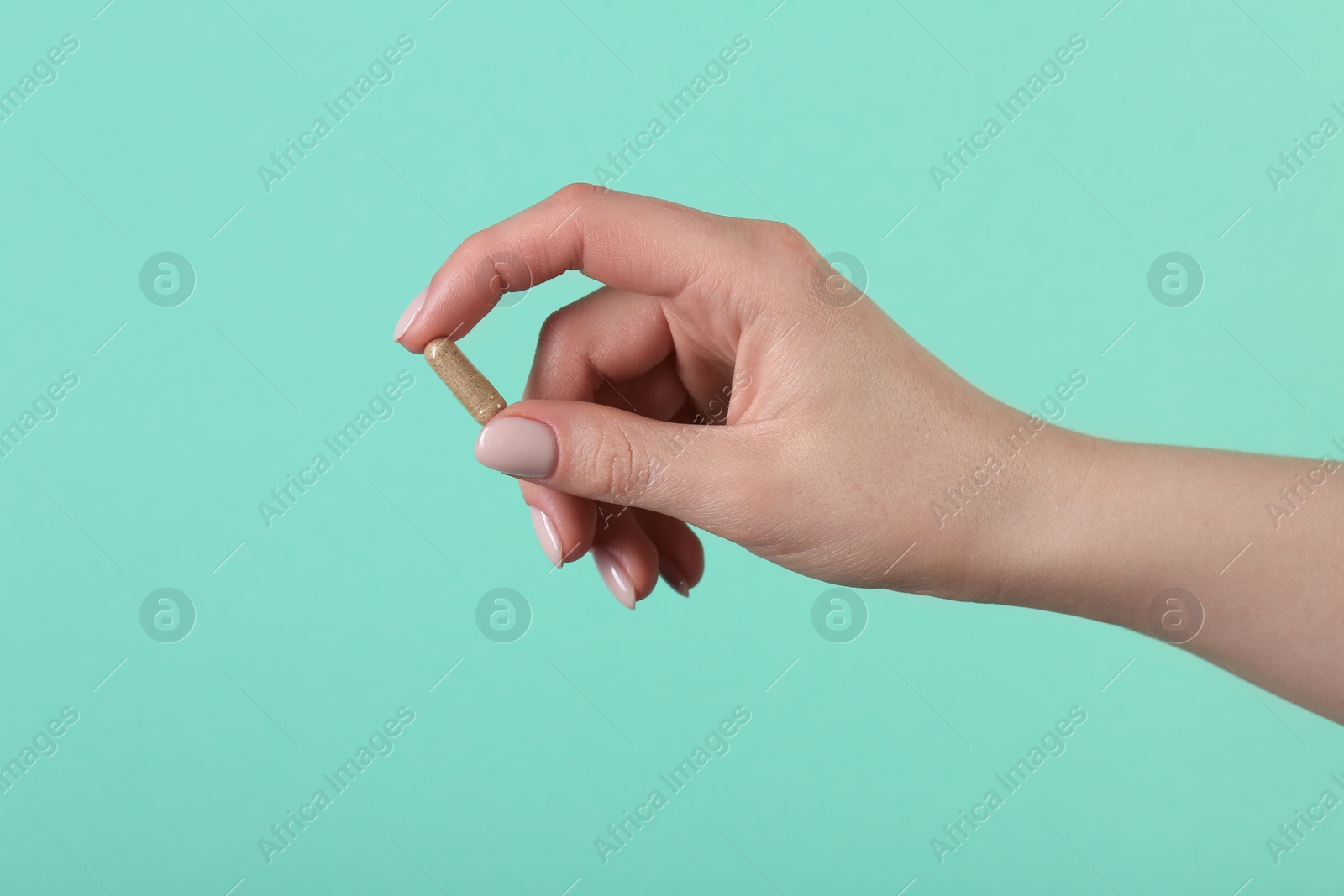 Photo of Woman holding vitamin capsule on turquoise background, closeup. Health supplement