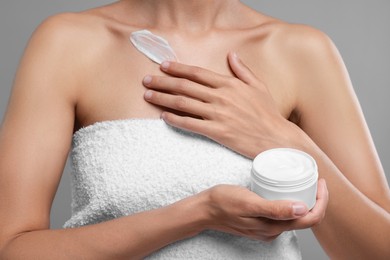 Photo of Woman applying cream onto body on grey background, closeup