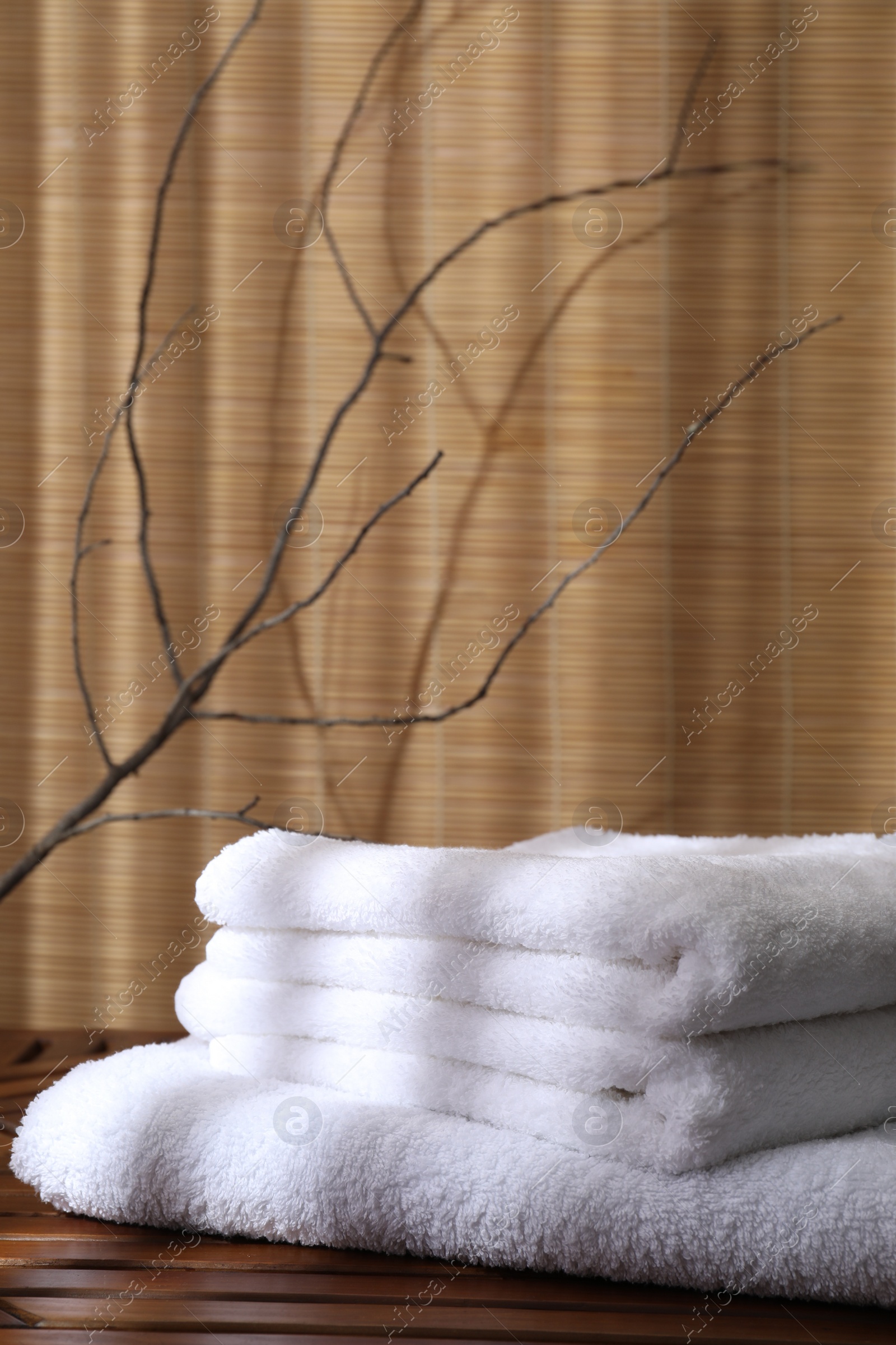 Photo of Stacked soft towels on wooden table and tree branches indoors