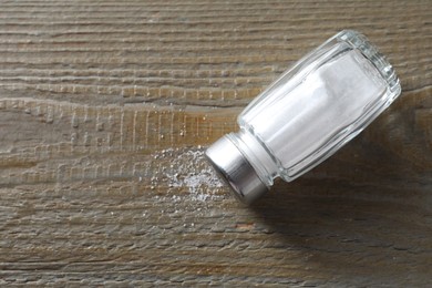 Photo of Organic salt in glass shaker on wooden table, top view. Space for text