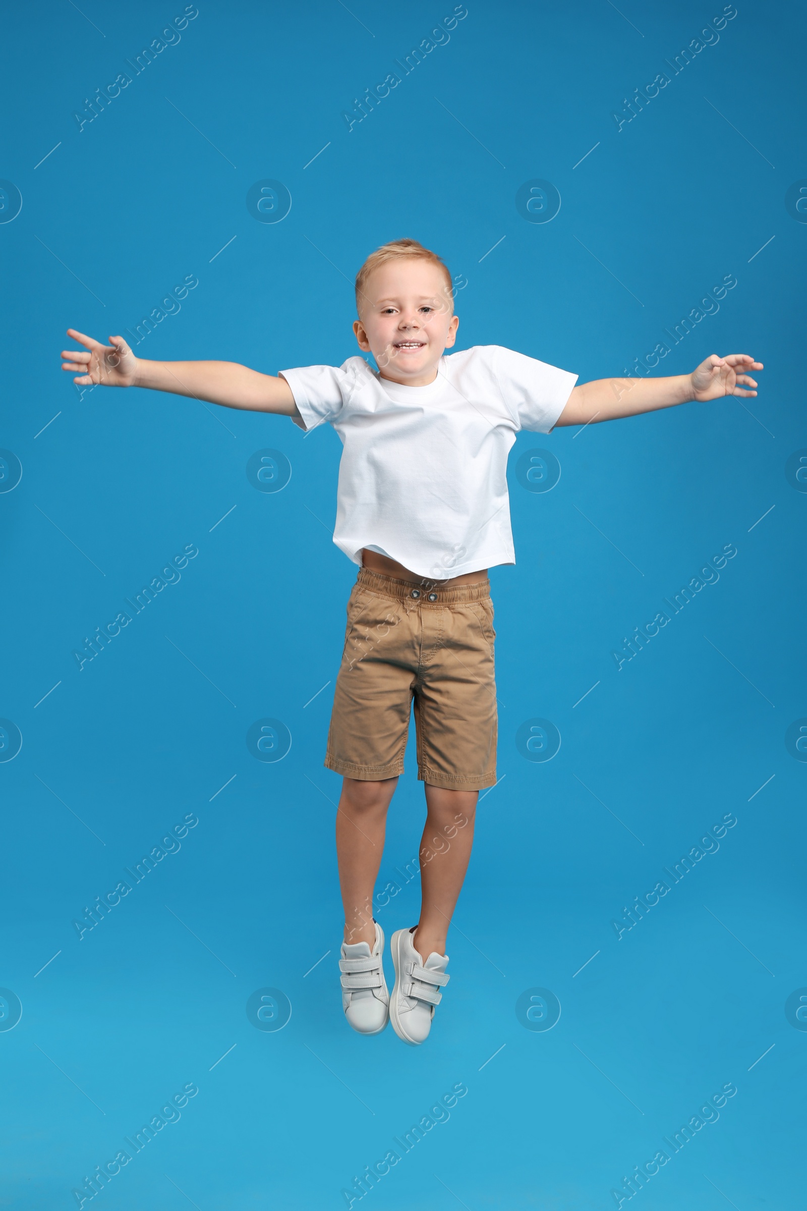 Photo of Cute little boy jumping on light blue background