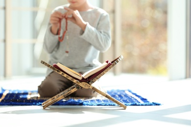 Book stand with Koran and little Muslim boy praying indoors