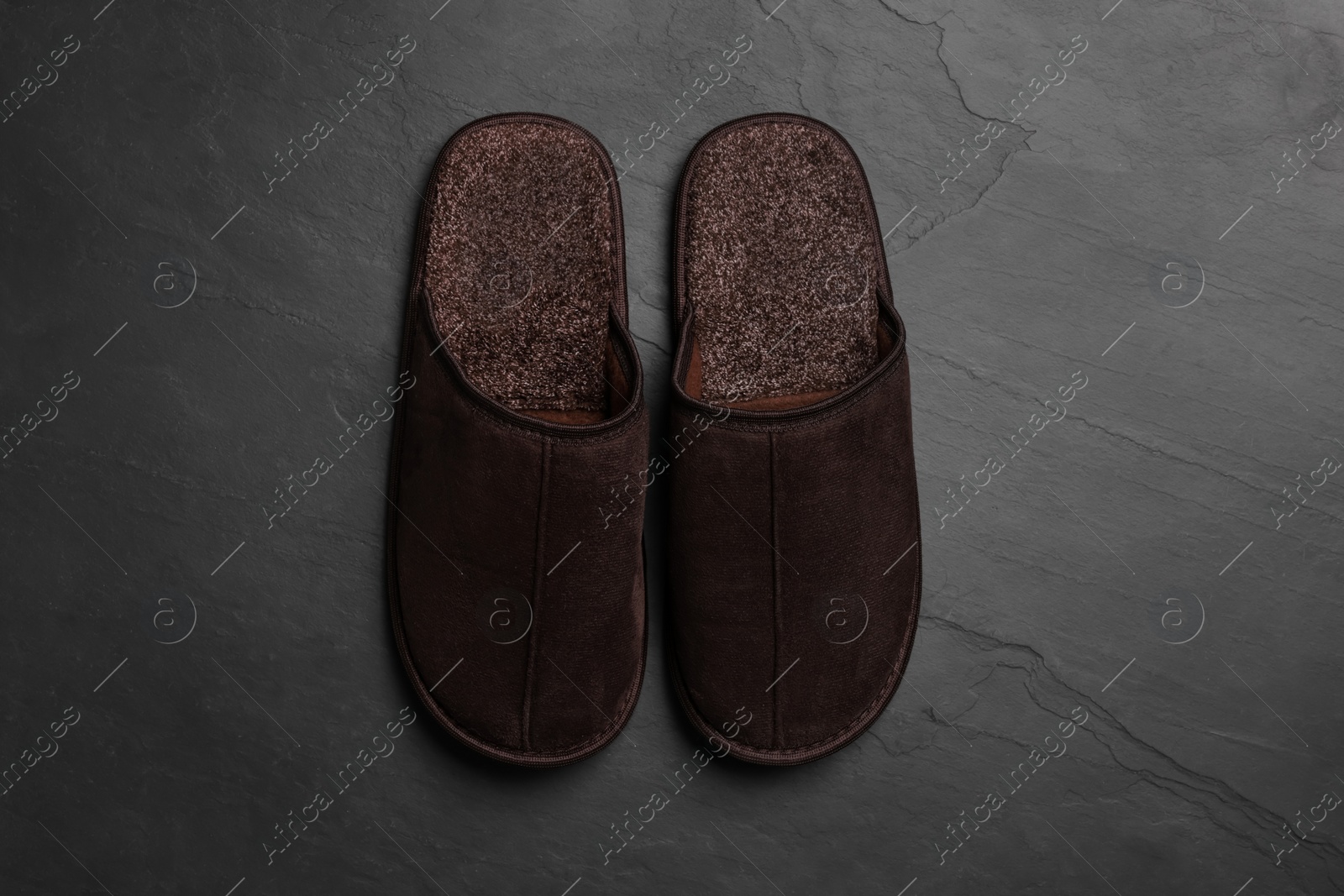 Photo of Pair of brown slippers on dark grey floor, top view