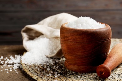 Photo of Pestle and mortar with natural sea salt on wooden table, closeup