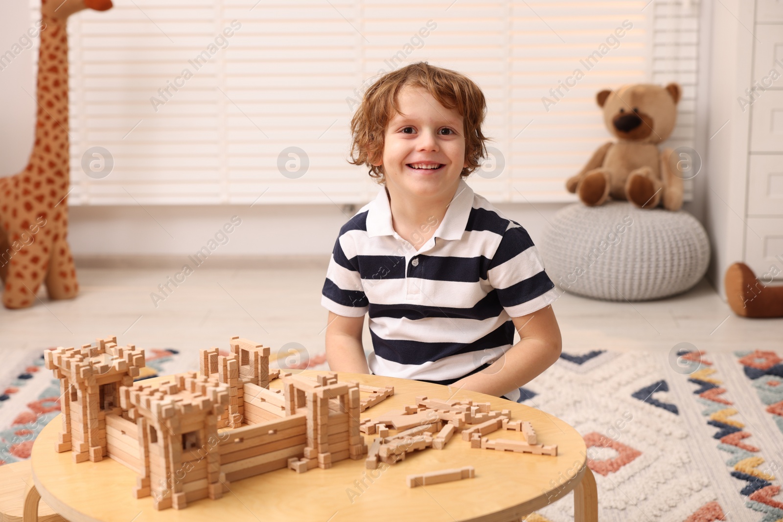 Photo of Cute little boy playing with wooden construction set at table in room. Child's toy