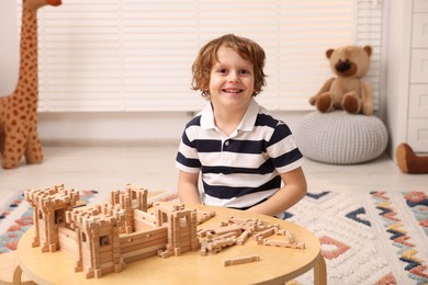 Photo of Cute little boy playing with wooden construction set at table in room. Child's toy