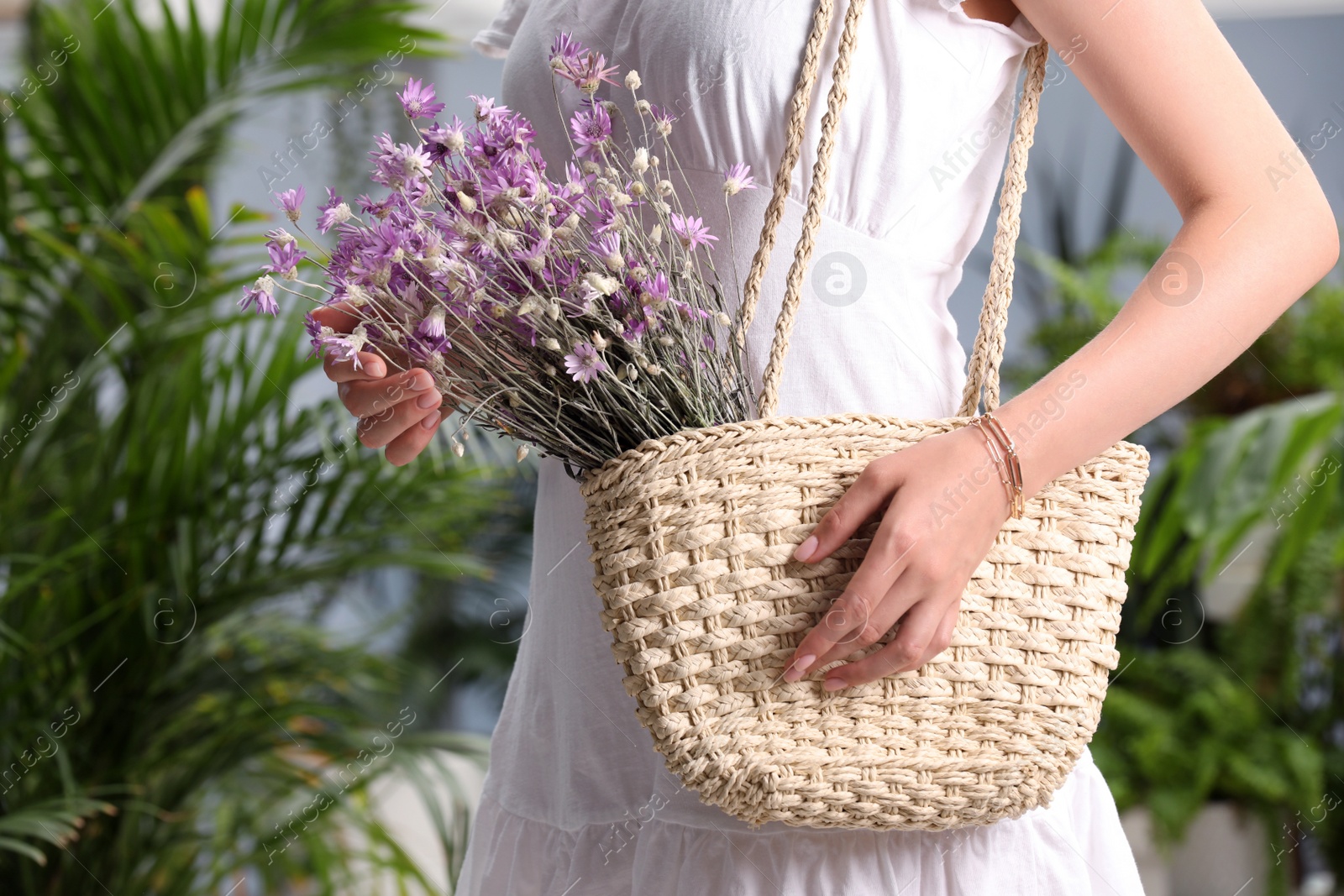 Photo of Woman holding beach bag with beautiful bouquet of wildflowers indoors, closeup