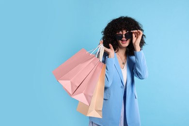 Photo of Happy young woman with shopping bags and stylish sunglasses on light blue background. Space for text