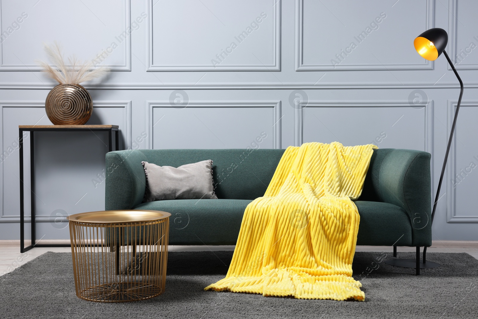 Photo of Comfortable sofa, blanket, side table and lamp in living room