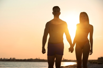 Photo of Young woman in bikini spending time with her boyfriend on beach at sunset. Lovely couple