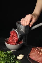 Woman making beef mince with manual meat grinder at table against black background, closeup