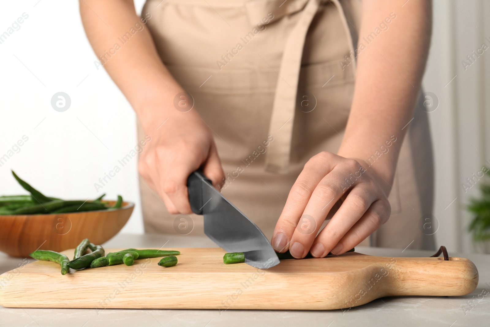 Photo of Woman cutting raw green beans for tasty dish at table