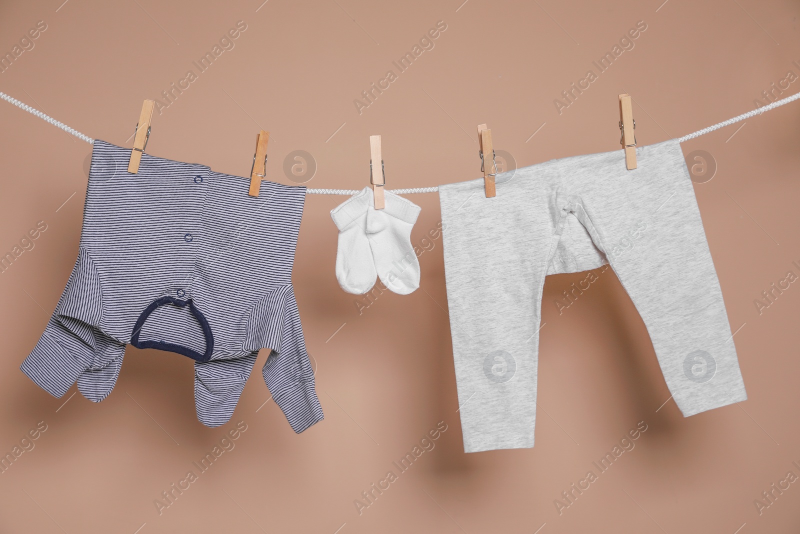 Photo of Cute small baby clothes hanging on washing line against brown background