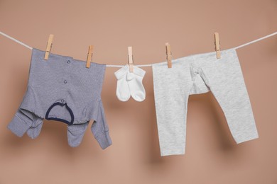 Photo of Cute small baby clothes hanging on washing line against brown background