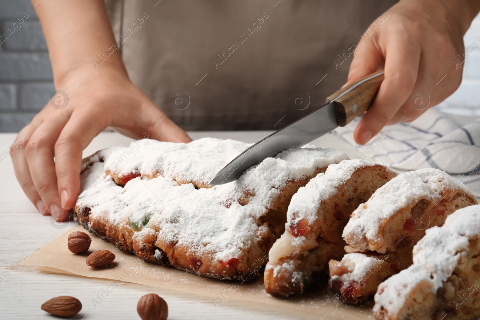 Photo of Woman cutting traditional Christmas Stollen with icing sugar at white wooden table, closeup