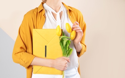 Stylish woman with clutch and spring flowers against color background, closeup