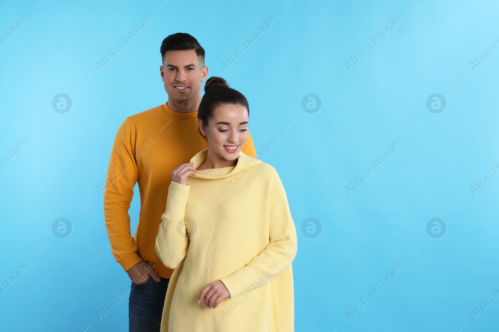 Photo of Happy couple wearing yellow warm sweaters on light blue background. Space for text