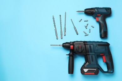 Photo of Modern electric power drill and different bits on light blue background, flat lay. Space for text