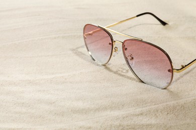 Photo of Stylish sunglasses on sand, closeup. Space for text