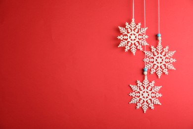 Photo of Beautiful decorative snowflakes hanging on red background, space for text