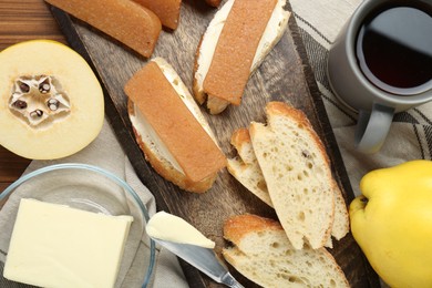 Delicious quince paste, bread, butter, cup of tea and fresh fruits on wooden table, flat lay