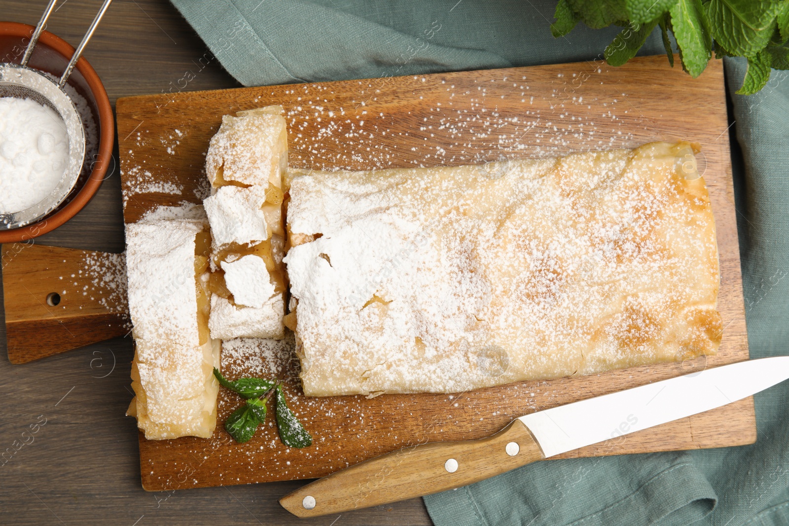 Photo of Delicious apple strudel with powdered sugar and mint on wooden table, flat lay