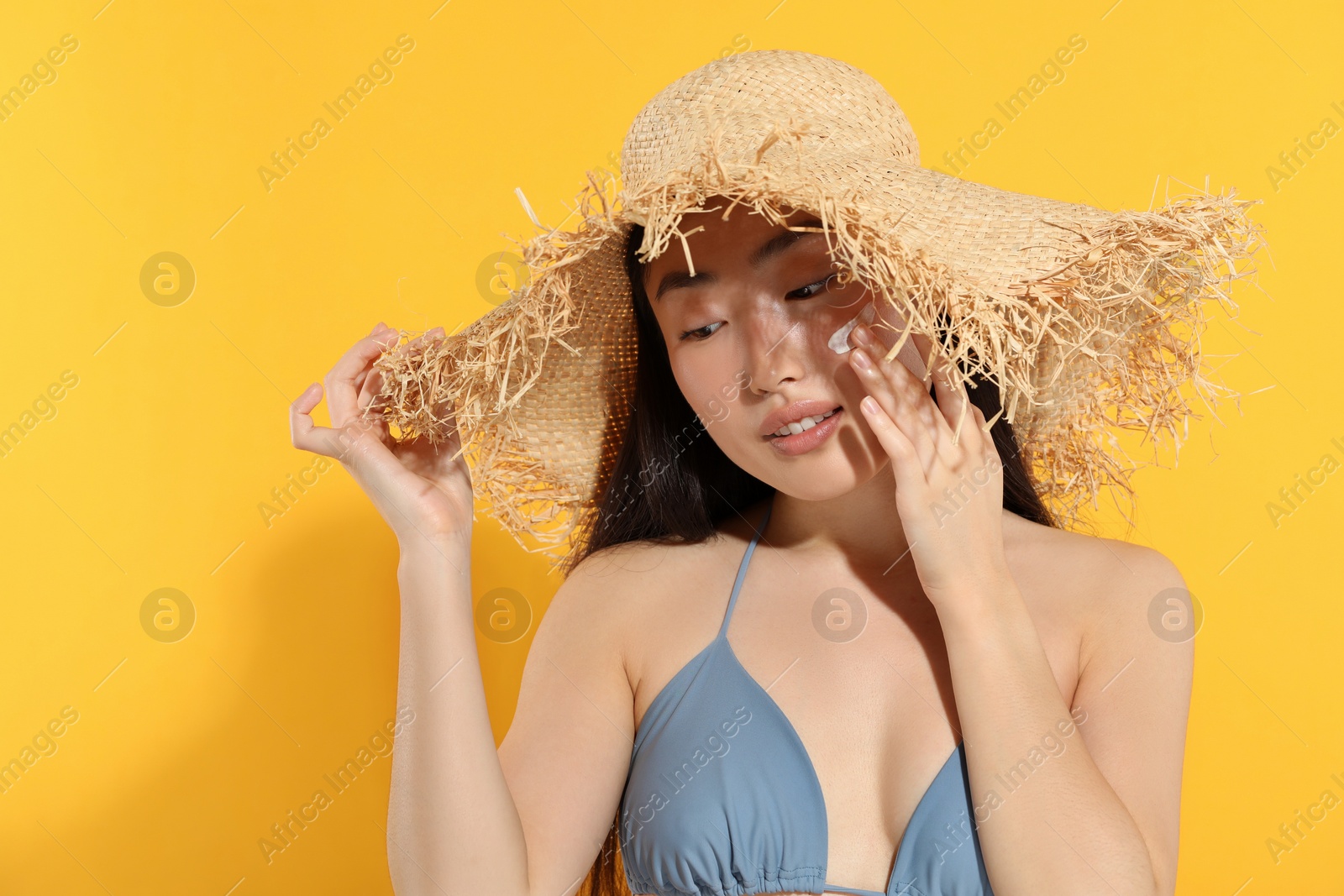 Photo of Beautiful young woman in straw hat with sun protection cream on her face against orange background, space for text