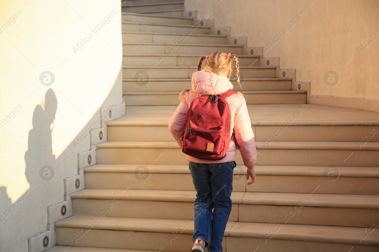 Photo of Cute little girl with backpack on stairs outdoors, back view