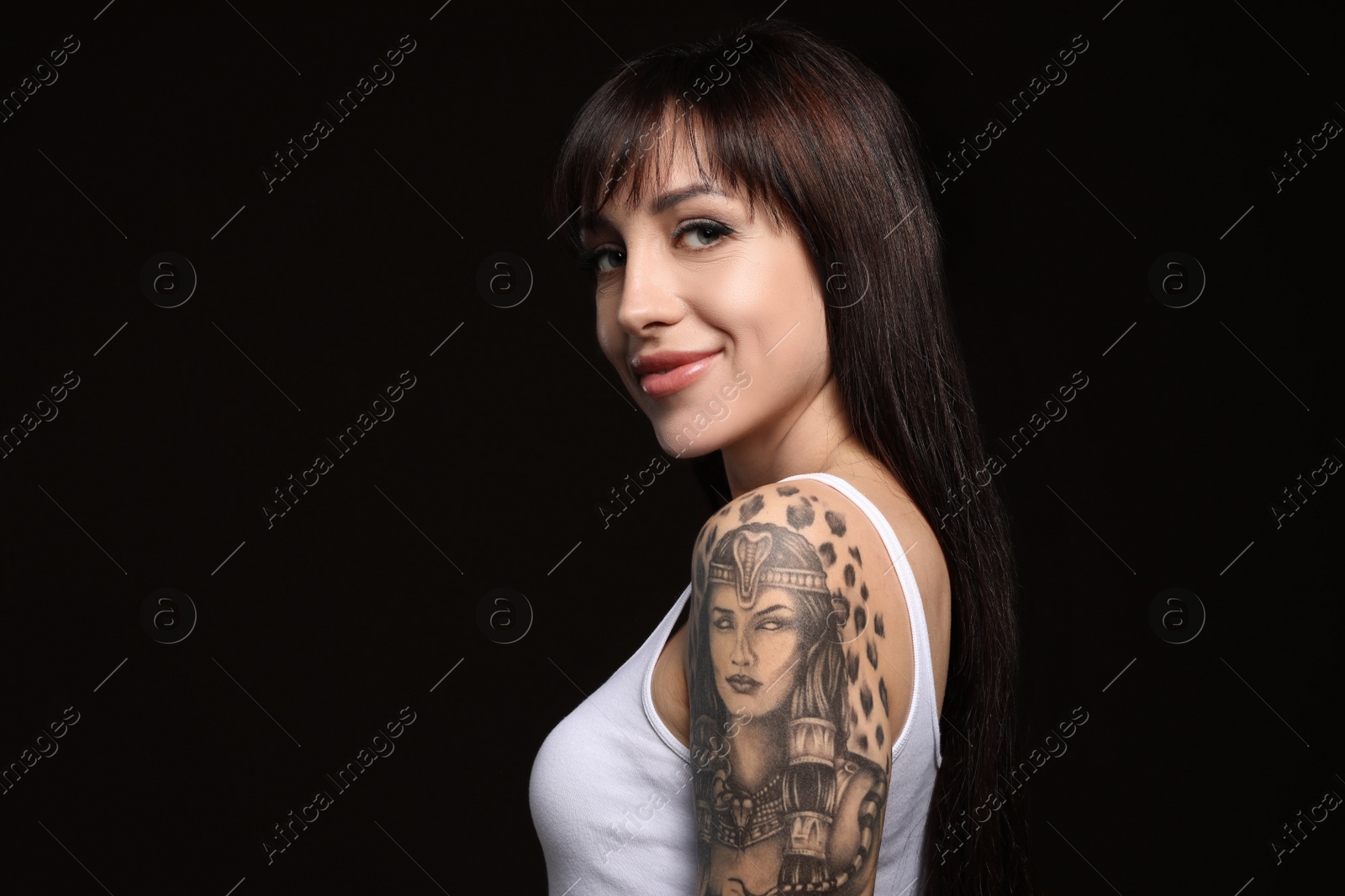 Photo of Beautiful woman with tattoos on arm against black background. Space for text