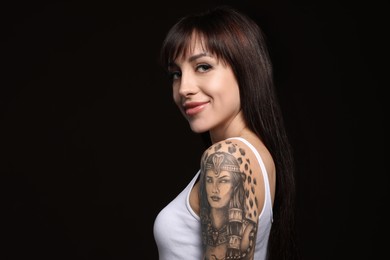 Beautiful woman with tattoos on arm against black background. Space for text