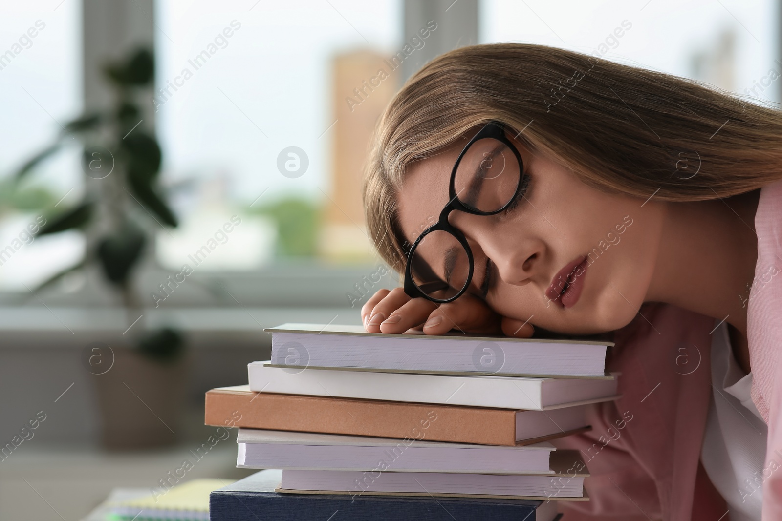 Photo of Young tired woman sleeping near books at white table indoors, closeup