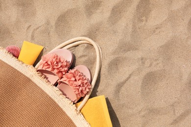 Photo of Stylish bag with beach accessories on sand, top view. Space for text