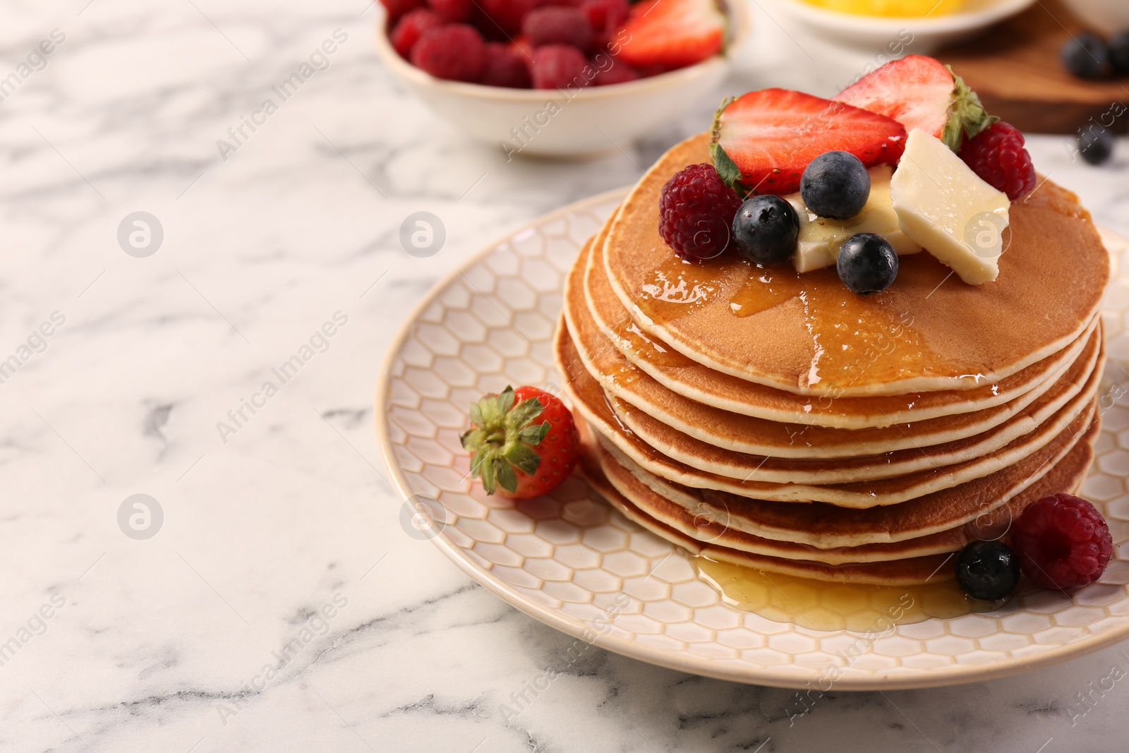 Photo of Delicious pancakes with fresh berries, butter and honey on white marble table, closeup. Space for text