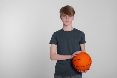 Photo of Teenage boy with basketball ball on light grey background. Space for text