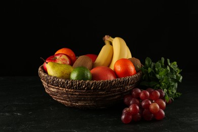 Photo of Fresh ripe fruits and wicker bowl on black table