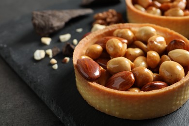 Photo of Tartlets with caramelized nuts on black table, closeup. Delicious dessert