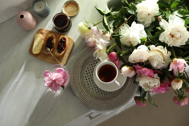 Photo of Beautiful peonies and breakfast on kitchen counter, flat lay