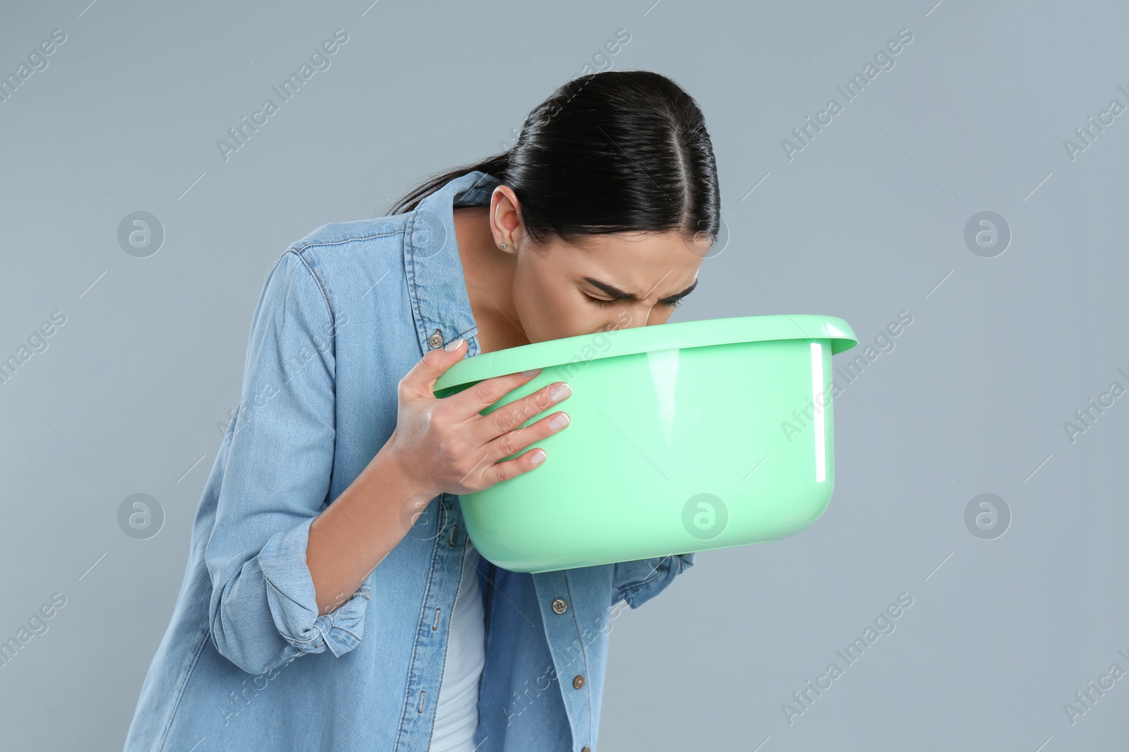 Photo of Woman with basin suffering from nausea on grey background. Food poisoning