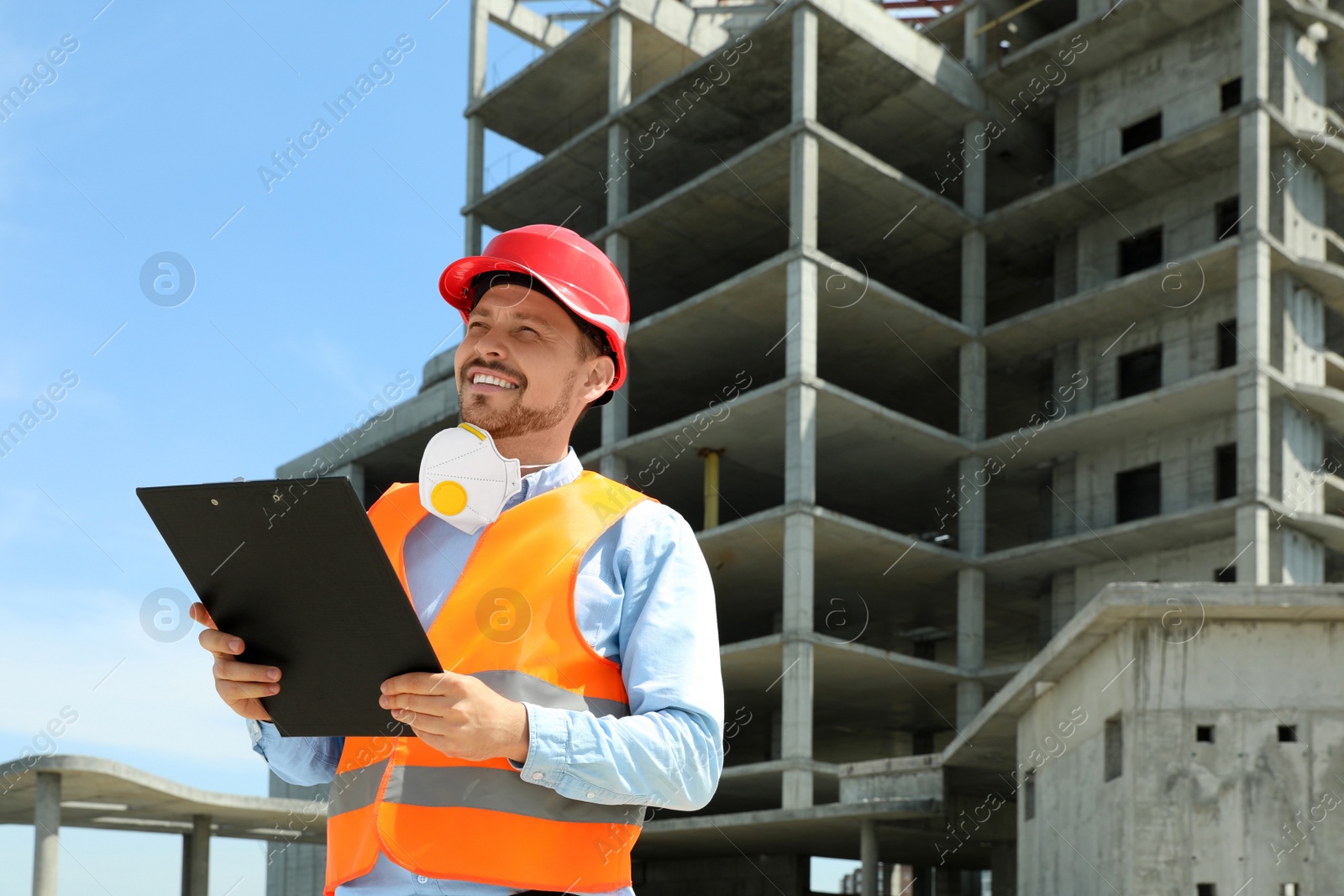 Photo of Professional engineer in safety equipment with clipboard at construction site. Space for text