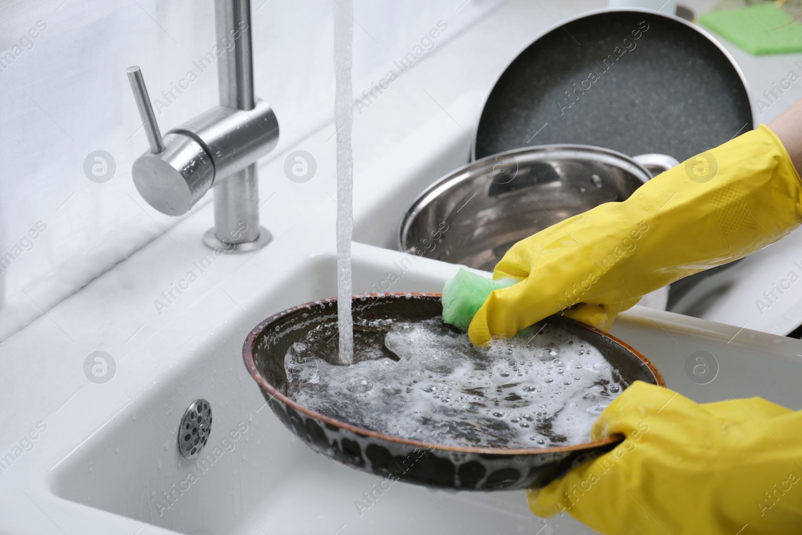 Photo of Woman washing frying pan with sponge in kitchen sink, closeup