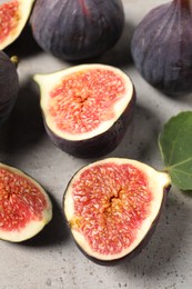 Photo of Whole and cut ripe figs on light grey textured table, closeup