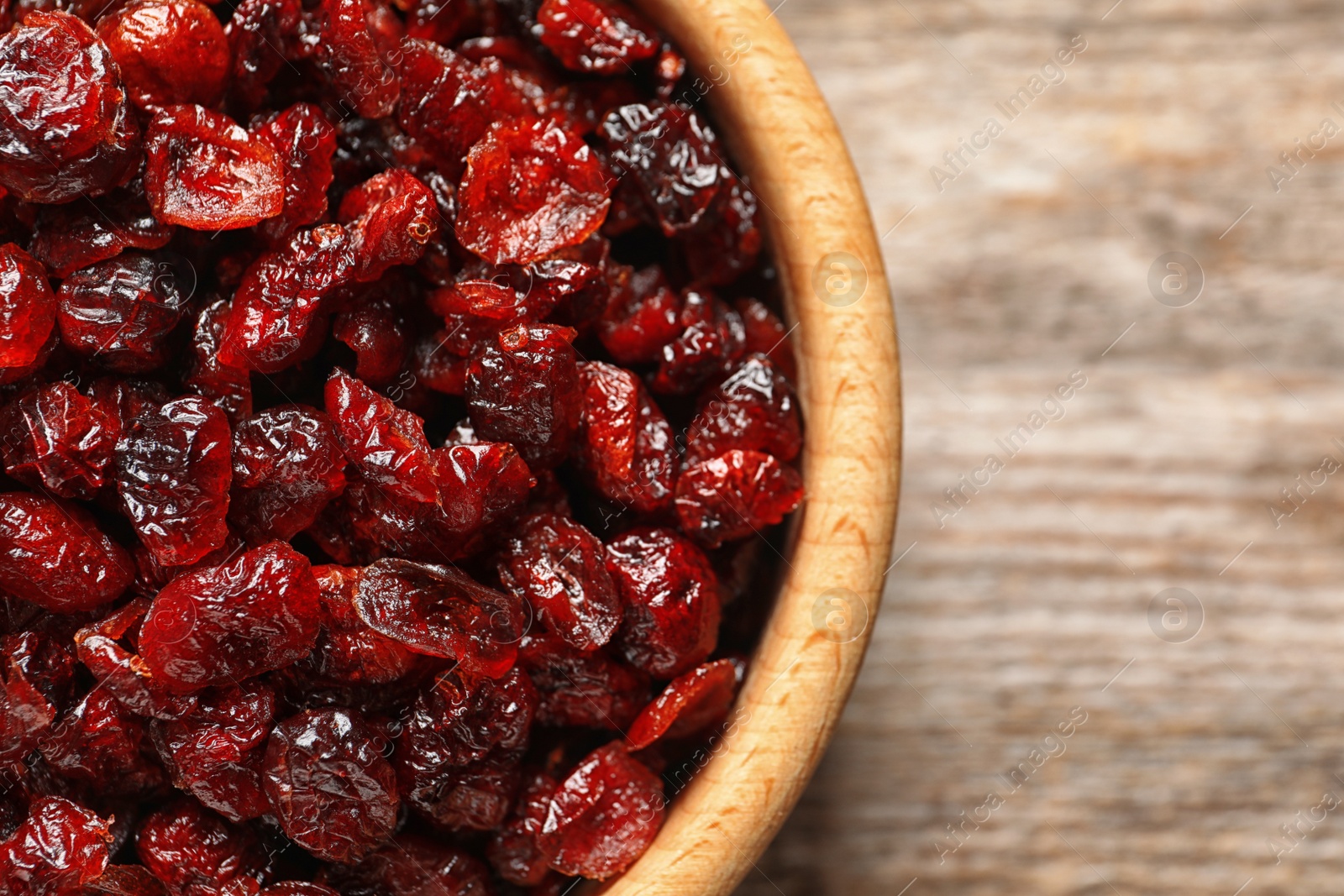 Photo of Bowl with cranberries on wooden background, top view. Dried fruit as healthy snack